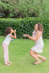 Latin Mother and daughter playing with bubbles in a park.