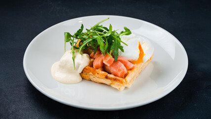 Breakfast Viennese waffles with salmon fish, poached egg, arugula and sauce.