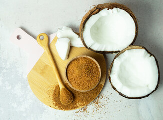 Coconut palm brown sugar in a wooden bowl and spoon and half of the coconut fruit on a gray concrete background.