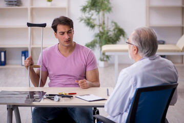 Fototapeta premium Young leg injured patient visiting old male doctor