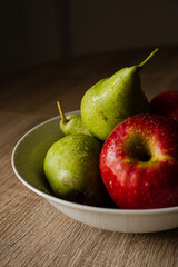 Bol de fruta con manzanas y peras sobre mesa de madera.