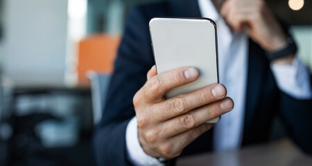 Male entrepreneur using smartphone at workplace, browsing business app or chatting with client, selective focus