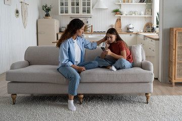Caring attentive mother stroking daughter sits on couch with phone in hands offers to take walk and...