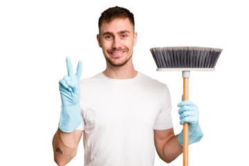 Young man holding a broom to clean his house cut out isolated showing number two with fingers.