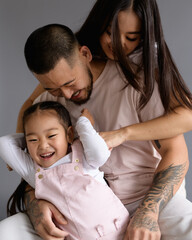 Happy young asian woman hugging husband and toddler kid isolated on grey 