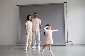 Smiling asian parents hugging while toddler daughter dancing on grey background 