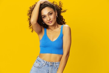 Woman with curly afro hair in a blue t-shirt on. yellow background signs with her hands, look into the camera, smile with teeth and happiness, copy space