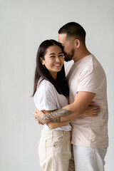 Smiling asian man hugging young wife isolated on grey background 