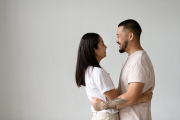 Profile of smiling asian couple hugging and looking at each other isolated on grey background 