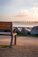 Isolated and empty public bench at sunrise. Bridge of the island of Re in background. peaceful or...
