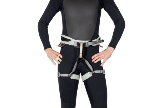 Man wearing a black wetsuit and gray climbing harness for canyoneering on a white isolated background with hands on hips. 