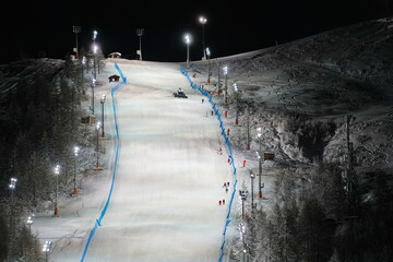 Scenic night view of an illuminated snowy ski track. Night skiing service at Sestriere winter...