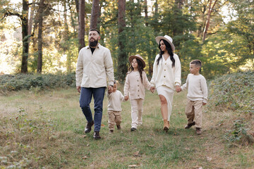 Naklejka na ściany i meble Young mother, father with daughter and sons are walking, having fun in autumn forest. Family holding hands enjoying time together at background of trees. Happy parenthood and childhood concept.