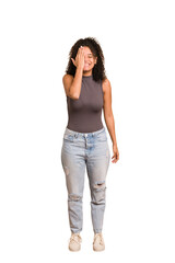 Young african american woman with curly hair cut out isolated having fun covering half of face with palm.