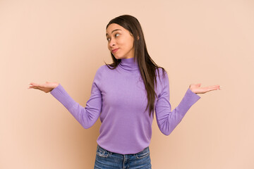 Young colombian woman isolated on beige background confused and doubtful shrugging shoulders to...