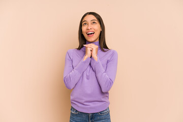 Young colombian woman isolated on beige background praying for luck, amazed and opening mouth looking to front.