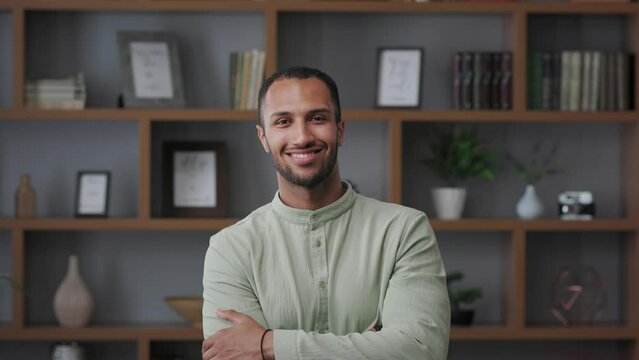 Business portrait of confident handsome mixed race man looking at camera and smiling. Young modern male leader, entrepreneur, manager indoors at workplace in office. Successful businessman.