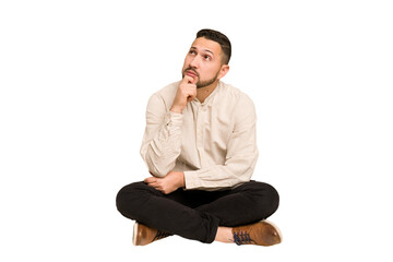 Adult latin man sitting on the floor cut out isolated looking sideways with doubtful and skeptical...