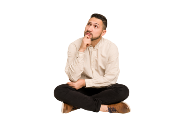 Adult latin man sitting on the floor cut out isolated looking sideways with doubtful and skeptical expression.