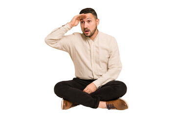 Adult latin man sitting on the floor cut out isolated looking far away keeping hand on forehead.