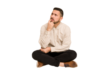 Adult latin man sitting on the floor cut out isolated looking sideways with doubtful and skeptical expression.