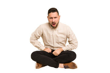 Adult latin man sitting on the floor cut out isolated shouting very angry, rage concept, frustrated.