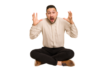 Adult latin man sitting on the floor cut out isolated screaming to the sky, looking up, frustrated.