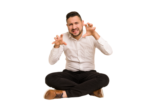 Adult latin man sitting on the floor cut out isolated showing claws imitating a cat, aggressive gesture.