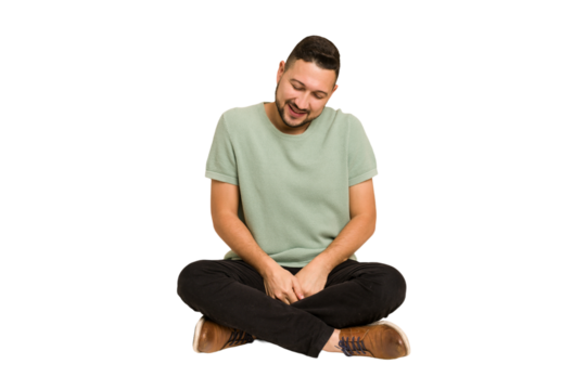 Adult latin man sitting on the floor cut out isolated laughs and closes eyes, feels relaxed and happy.