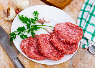 Shaped patties for burgers from raw ground beef meat with fresh parsley sprigs, spicy garlic and allspice on plate. Cooking ingredients