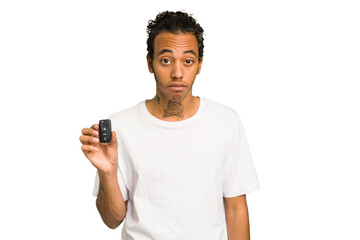 Young African American man holding car keys isolated shrugs shoulders and open eyes confused.
