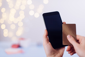 St. Valentine's Day online shopping, searching on smartphone for gifts. Credit card and heart in hands, close-up. Copy space on the screen . 