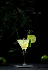Gimlet alcoholic cocktail with dry gin, liqueur, lime juice and ice in glass garnished with lime zest. Black background