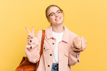 Young student woman holding a brain isolated on yellow background joyful and carefree showing a...