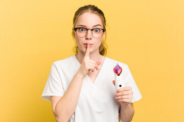 Young beautician woman holding a facial cleaner isolated on yellow background keeping a secret or asking for silence.