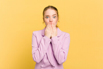 Young caucasian redhead woman isolated on yellow background shocked, covering mouth with hands, anxious to discover something new.