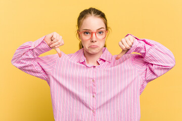 Young caucasian redhead woman isolated on yellow background showing a dislike gesture, thumbs down....