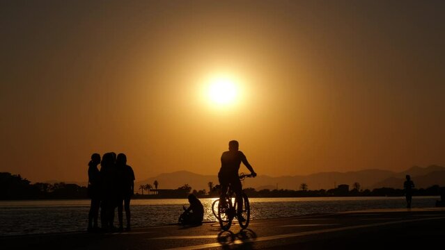 Sunset on the embankment. Silhouette of girls taking pictures at sunset, a bicycle passing by, a girl with a smartphone and a bicycle.