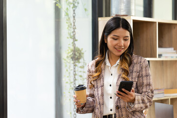 Asian business girl in her workstation at holding coffee cup and smartphone while smile
