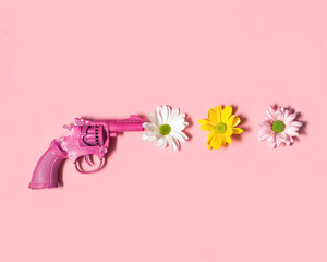 Colorful flowers and gun on pastel light pink background. Minimalistic love concept. Creative peace flat lay idea.