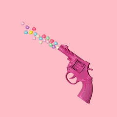 Colorful hearts and gun on pastel light pink background. Minimalistic love concept. Creative Valentine's Day flat lay idea.