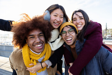 Happy multiracial young friends standing together outdoor smiling at camera. International friendship concept with group of four millennial people from diverse cultures having fun together