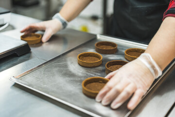 A baker with transparent gloves placing tarts on a baking tray. Blurred background. . High quality photo