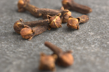 Brown dried cloves, textured on a gray stone background.
