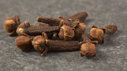 Brown dried cloves, textured on a gray stone background.