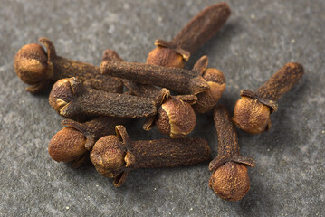 Brown dried cloves, textured on a gray stone background.