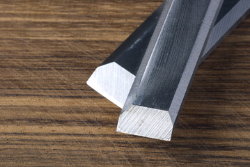 Steel silver carpenter's chisels on brown wood grain background.
