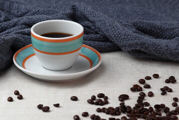 Colorful cup of black coffee, cozy warm blanket and coffee beans spread in the bottom right corner.