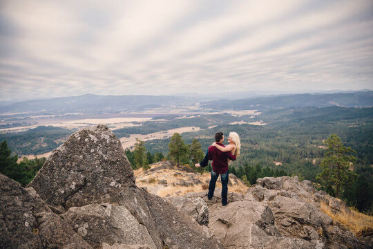 A man holds his fiance in both arms atop a rocky outcropping at Spencers Butte Oregon