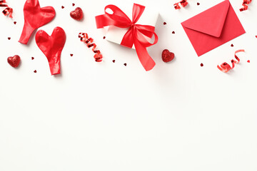 Valentine's Day background. Gift box with red ribbon bow, candy, confetti, envelope on white background. Valentines day card. Flat lay, top view.